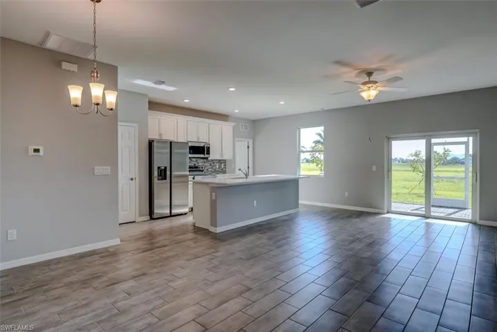 Kitchen featuring ceiling fan with notable chandelier, a center island with sink, appliances with stainless steel finishes, hanging light fixtures, and decorative backsplash