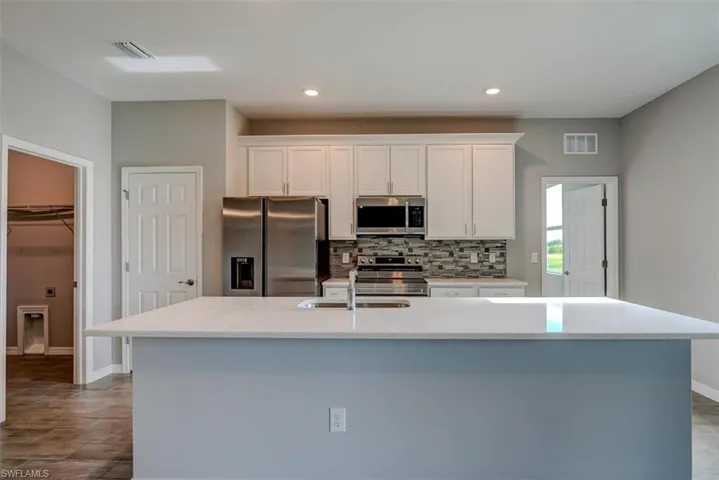 Kitchen featuring a kitchen island with sink, appliances with stainless steel finishes, white cabinetry, and sink