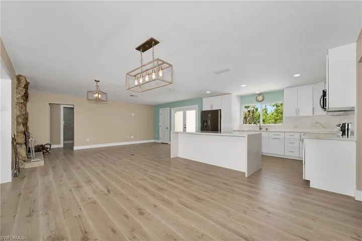 Kitchen featuring open floor plan, light wood finished floors, white cabinets, light countertops, and decorative backsplash