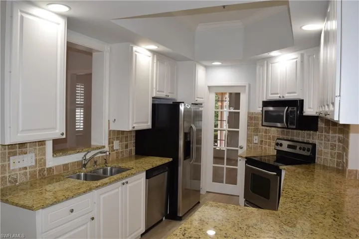 Kitchen featuring crown molding, white cabinets, sink, stainless steel appliances, and light stone counters