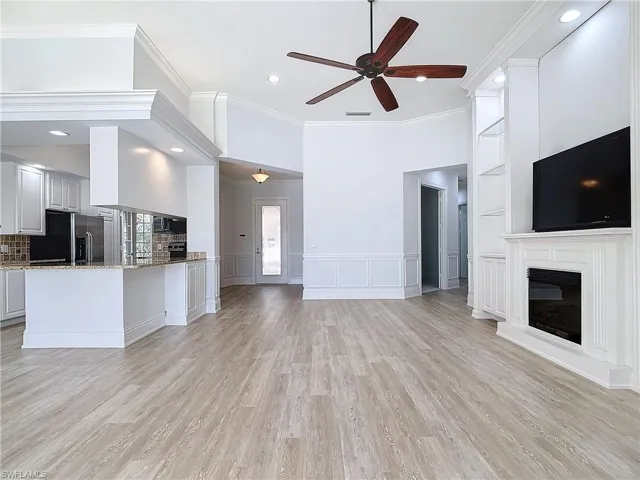 Unfurnished living room featuring crown molding, built in shelves, ceiling fan, and light wood-type flooring