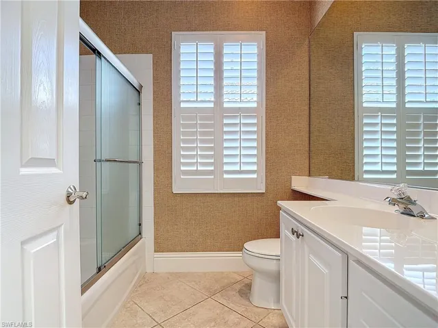 Full bathroom with shower / bath combination with glass door, vanity, toilet, and tile patterned flooring