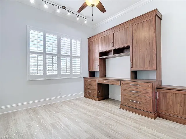 Unfurnished office with ornamental molding, built in desk, ceiling fan, and light hardwood / wood-style floors