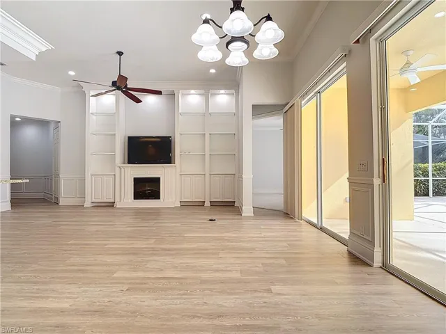 Unfurnished living room featuring crown molding, ceiling fan with notable chandelier, and light wood-type flooring