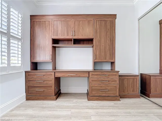 Unfurnished office featuring crown molding, built in desk, and light wood-type flooring
