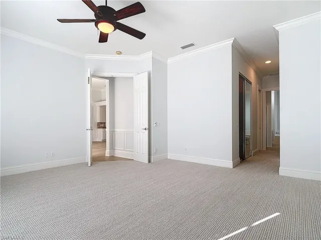Empty room with ceiling fan, light colored carpet, and ornamental molding