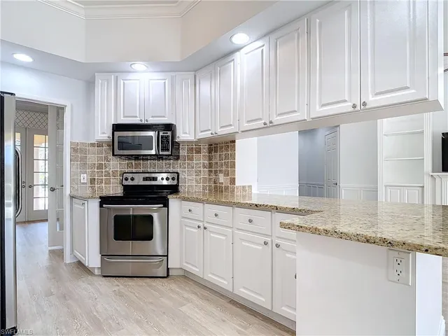Kitchen with white cabinetry, stainless steel appliances, light stone countertops, ornamental molding, and kitchen peninsula