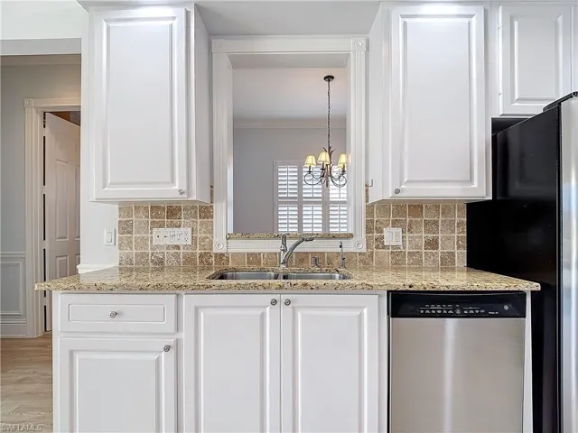 Kitchen with white cabinetry, sink, stainless steel dishwasher, and light stone counters