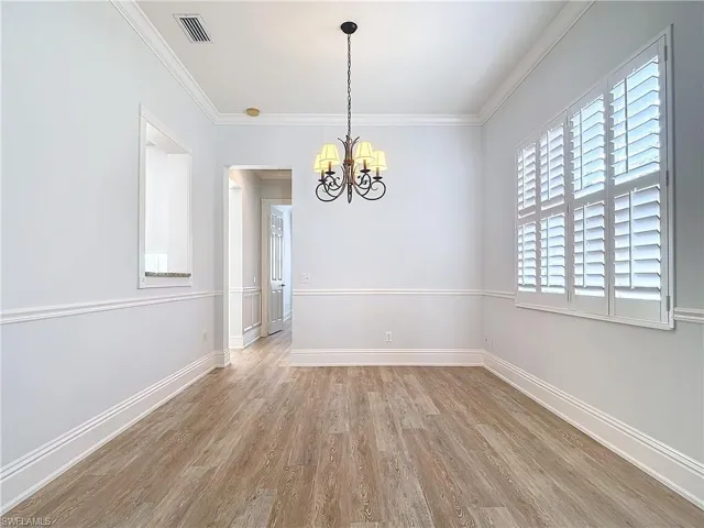 Spare room with an inviting chandelier, crown molding, light hardwood / wood-style flooring, and a healthy amount of sunlight