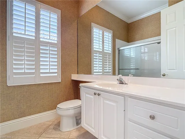 Bathroom featuring toilet, crown molding, vanity, a shower with door, and tile patterned flooring