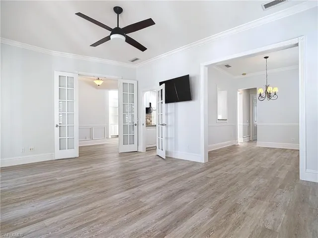 Unfurnished room with crown molding, hardwood / wood-style flooring, ceiling fan with notable chandelier, and french doors