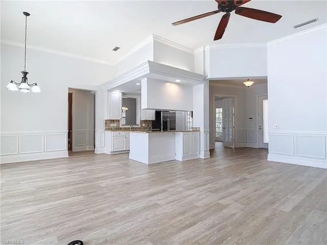 Unfurnished living room featuring crown molding, ceiling fan with notable chandelier, and light wood-type flooring