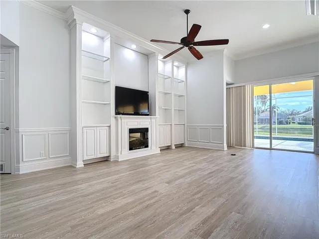 Unfurnished living room featuring crown molding, built in shelves, and light wood-type flooring
