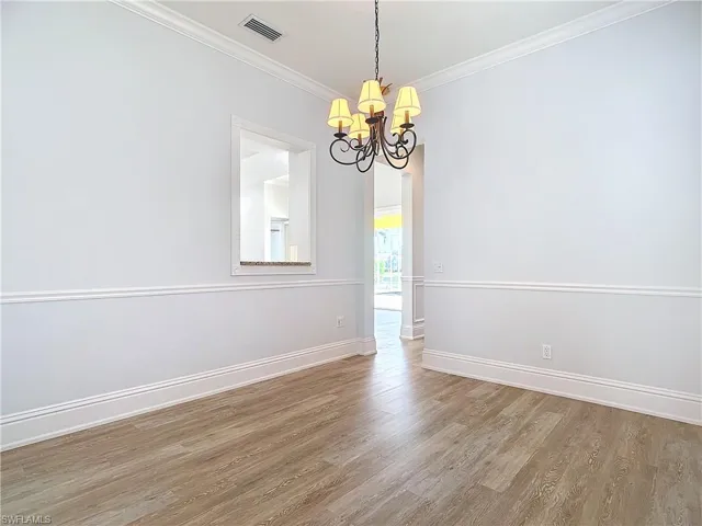 Unfurnished room featuring an inviting chandelier, ornamental molding, and hardwood / wood-style flooring