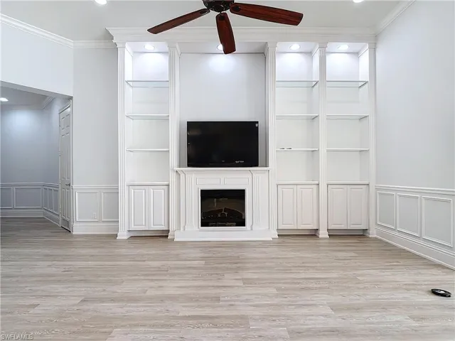 Unfurnished living room featuring ornamental molding, light hardwood / wood-style floors, ceiling fan, and built in shelves