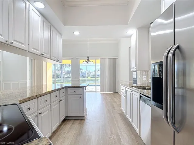 Kitchen featuring decorative light fixtures, tasteful backsplash, white cabinets, light stone counters, and stainless steel appliances