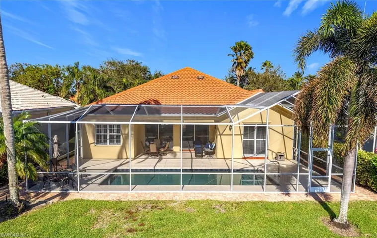 Rear view of property featuring glass enclosure, a patio area, and a lawn