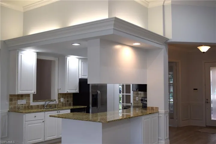 Kitchen featuring dark stone counters, white cabinetry, kitchen peninsula, and tasteful backsplash