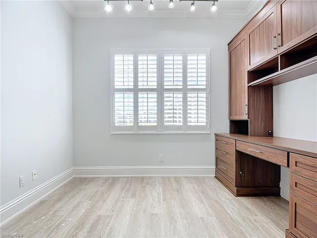 Unfurnished office featuring crown molding, built in desk, and light hardwood / wood-style flooring