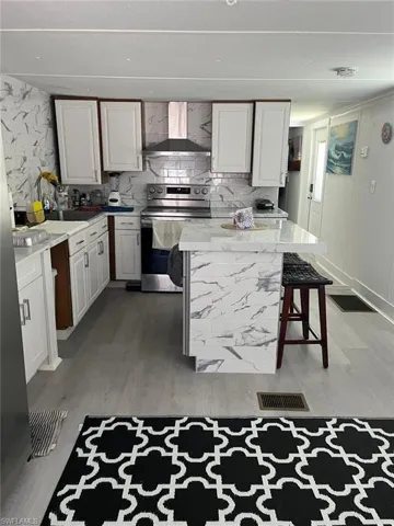 Kitchen featuring white shaker cabinetry, an island with seating, stainless steel appliances, a subway tile backsplash, and light wood-finish flooring