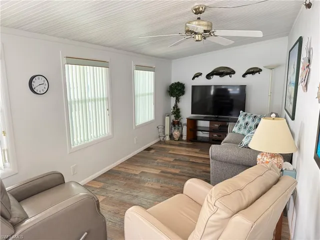 Living room with dark wood-type flooring, a ceiling fan, and ornamental molding