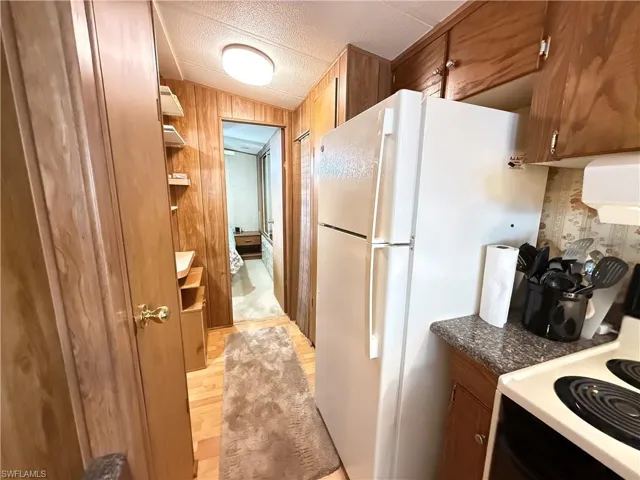 Kitchen with white appliances, brown cabinetry, dark countertops, open shelves, and exhaust hood