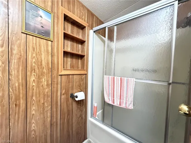 Bathroom with built in shelves and bath / shower combo with glass door