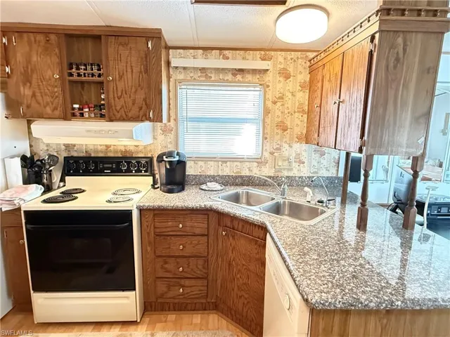 Kitchen with range with electric cooktop, brown cabinetry, dishwasher, under cabinet range hood, and open shelves