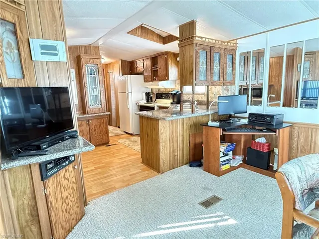 Kitchen with brown cabinetry, a peninsula, wooden walls, freestanding refrigerator, and light wood-style floors