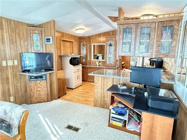 Kitchen with wood walls, lofted ceiling, light stone counters, black microwave, and light colored carpet