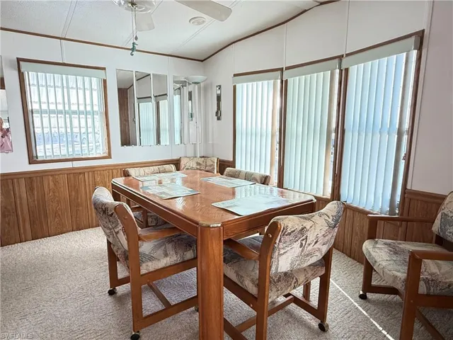 Dining space featuring wood walls, wainscoting, light colored carpet, a ceiling fan, and lofted ceiling