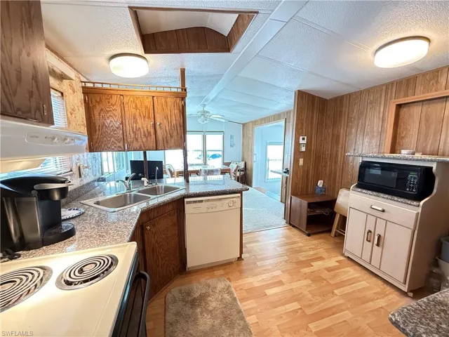 Kitchen featuring white appliances, a textured ceiling, a peninsula, ceiling fan, and wooden walls