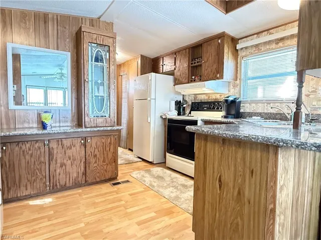Kitchen featuring range with electric stovetop, light wood finished floors, freestanding refrigerator, brown cabinets, and wooden walls