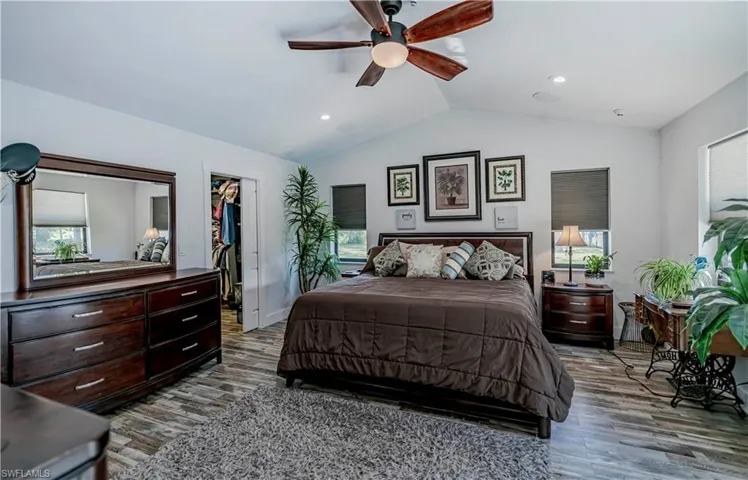 Bedroom featuring lofted ceiling, wood finished floors, multiple windows, a walk in closet, and recessed lighting