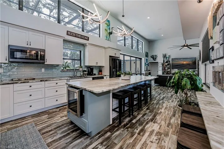 Kitchen featuring dark wood finished floors, beverage cooler, white cabinets, backsplash, and a kitchen breakfast bar