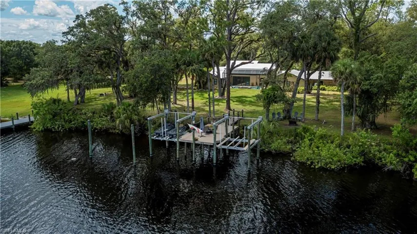 Dock featuring a water view, boat lift, a lawn, and view of scattered trees