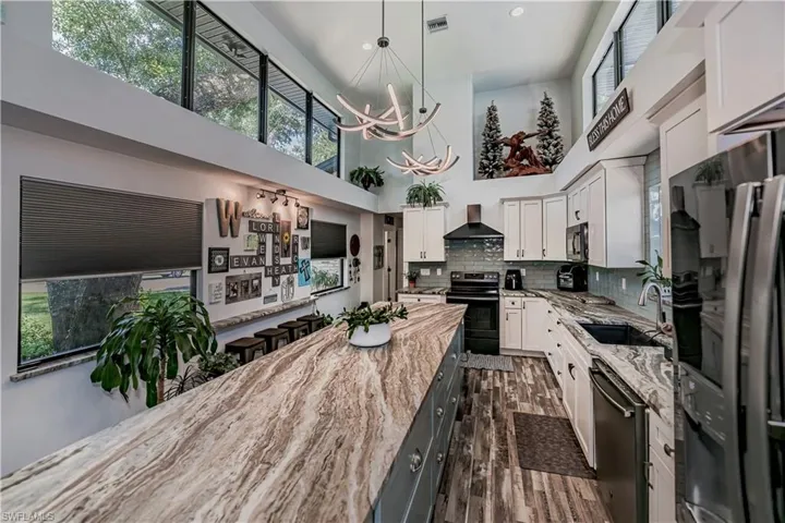 Kitchen featuring electric range, freestanding refrigerator, a chandelier, dishwashing machine, and a high ceiling