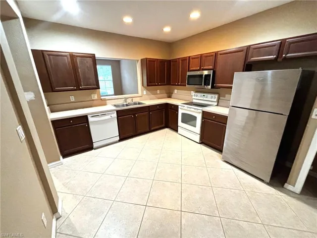 Kitchen with stainless steel appliances, dark wood finish cabinets, light countertops, recessed lighting, and light tile patterned floors