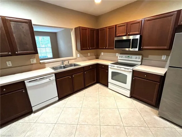 Kitchen featuring stainless steel appliances, light countertops, dark wood finish cabinetry, and light tile patterned floors