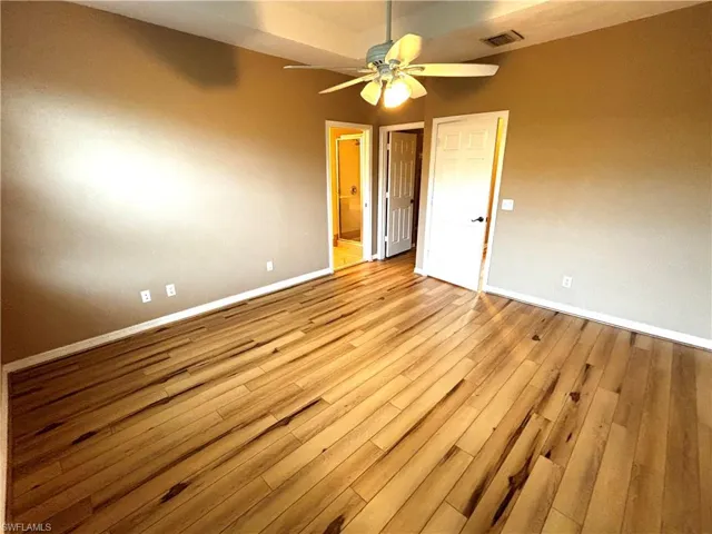 Unfurnished bedroom featuring hardwood / wood-style flooring, connected bathroom, and ceiling fan