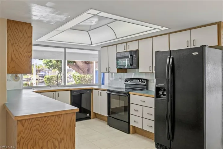 Kitchen with black appliances, light tile patterned flooring, white cabinetry, backsplash, and sink