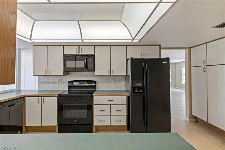 Kitchen with white cabinetry, black appliances, light tile patterned floors, and tasteful backsplash
