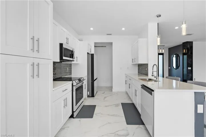 Kitchen with appliances with stainless steel finishes, white cabinets, light stone countertops, light marble finish flooring, and recessed lighting