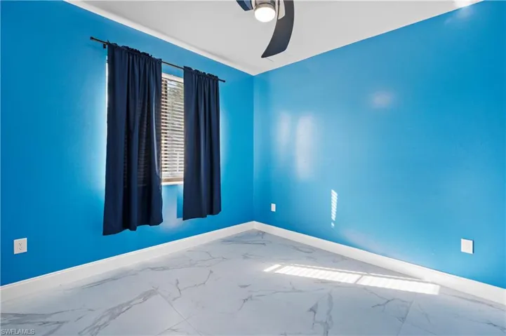 Empty room featuring marble look tiles and ceiling fan