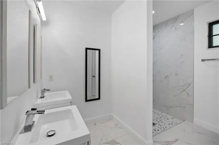 Full bathroom featuring light marble finish flooring, a marble finish shower, and two vanities