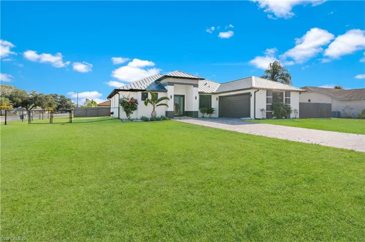 View of front of property featuring an attached garage, decorative driveway, a metal roof, a gate, and stucco siding