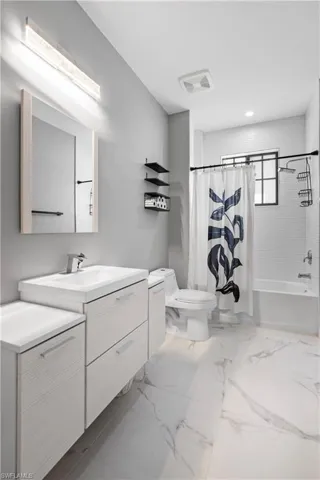 Bathroom featuring shower / tub combo with curtain, vanity, and light marble finish flooring