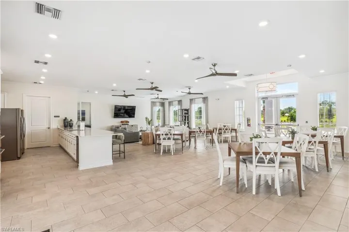 Spacious open-concept room featuring light-toned tile flooring, recessed lighting, multiple ceiling fans, large windows, and a central kitchen island with built-in cabinetry