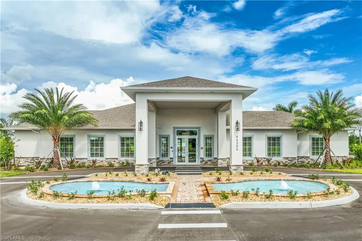 Stucco facade building with stone accents, a covered entry, dual water features with fountains, manicured landscaping, and twin palm trees
