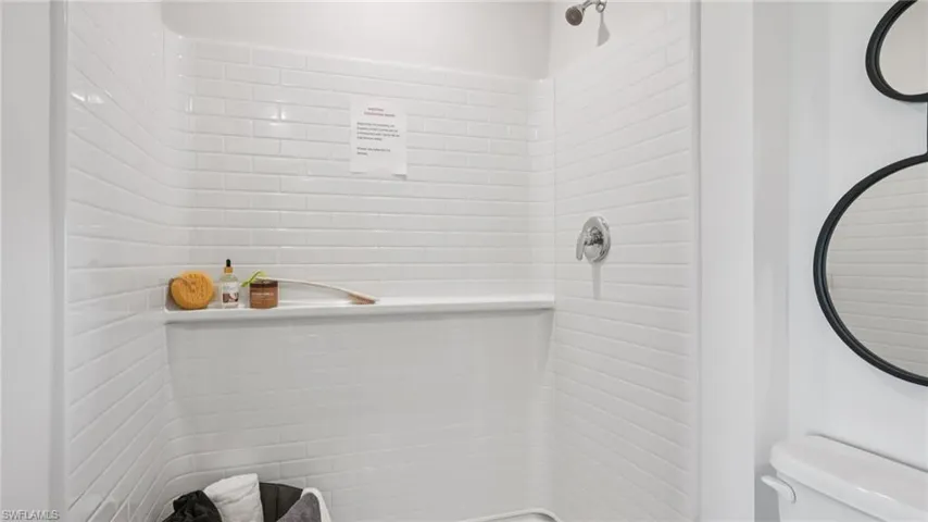 Shower stall with subway tile-style surround, built-in shelving, chrome fixtures, and a curved shower rod